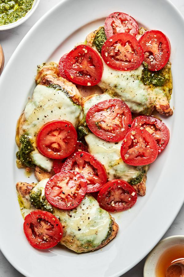 chicken caprese on a serving platter topped with pesto, melted mozzarella, roma tomatoes and drizzled with honey