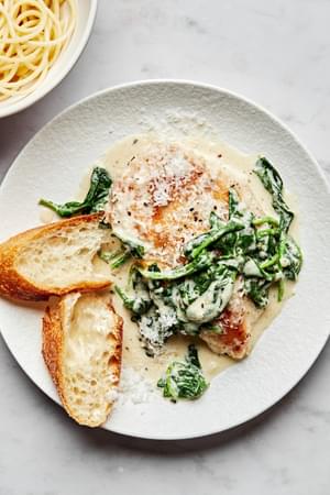 Chicken Florentine with cooked spinach in a white wine cream sauce topped with parmesan on a plate served with crusty bread