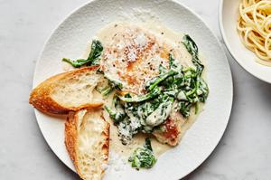 Chicken Florentine with cooked spinach in a white wine cream sauce topped with parmesan on a plate served with crusty bread