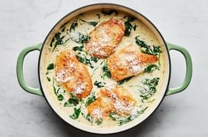 Chicken Florentine with cooked spinach in a rich white wine cream sauce topped with parmesan in a skillet