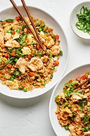 a bowl of chicken fried rice made with carrots, onions, peas, green onions, eggs, and soy sauce with chop sticks