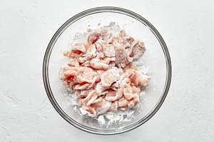 sliced raw chicken, seasoned with salt, tossed in corn starch in a glass bowl