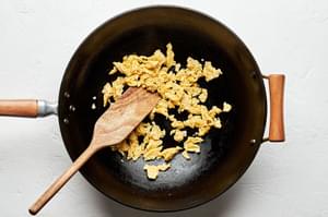 eggs mixed with coconut aminos, sesame oil and salt being cooked in a wok with a wooden spoon