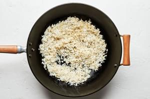 white rice being cooked in vegetable oil and sesame oil in a wok