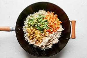 rice, chicken, carrots, onions, peas and green onions in a wok to make chicken fried rice