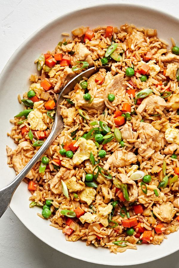 a bowl of chicken fried rice made with carrots, onions, peas, green onions, eggs, soy sauce, coconut aminos and sesame oil