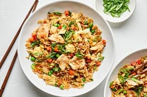 a bowl of chicken fried rice made with carrots, onions, peas, green onions, eggs, and soy sauce with chop sticks