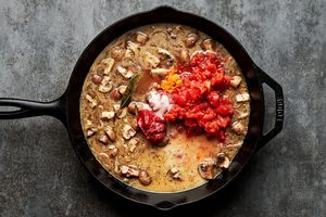 chicken marengo sauce being cooked in a skillet made with mushrooms, shallots, stock, tomato paste, orange zest & spices