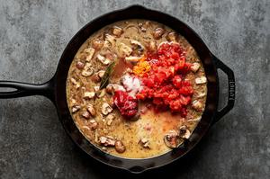 chicken marengo sauce being cooked in a skillet made with mushrooms, shallots, stock, tomato paste, orange zest & spices