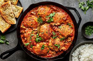 chicken marengo in a skillet topped with fresh parsley next to bowls of white rice and garlic bread