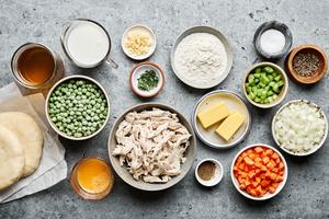 ingredients to make chicken pot pie in separate bowls: shredded chicken, vegetables, broth, spices, butter, milk & pie crust