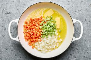 Carrots, onions, and celery cooking in melted butter in a pot, softening and sizzling as they prepare for chicken pot pie