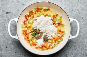 flour added to a pot with softened carrots, onions, and celery cooked in melted butter
