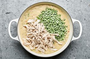 Chicken and peas being added to a pot filled with homemade chicken pot pie filling with vegetables and a creamy sauce