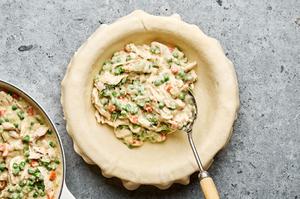 a pie crust being filled with chicken and vegetables in a creamy sauce