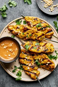 Grilled chicken satay skewers served with creamy peanut sauce, garnished with cilantro and crushed peanuts