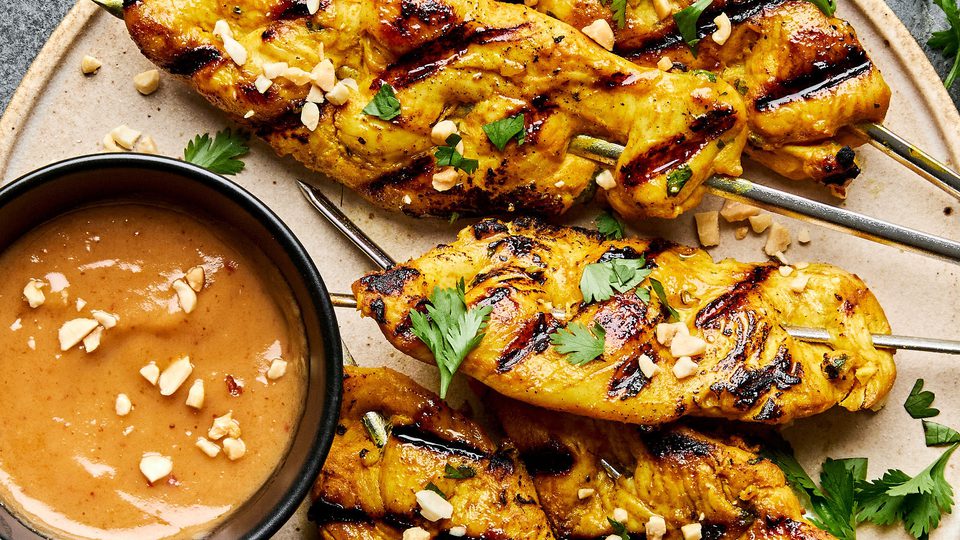 Grilled chicken satay skewers served with creamy peanut sauce, garnished with cilantro and crushed peanuts