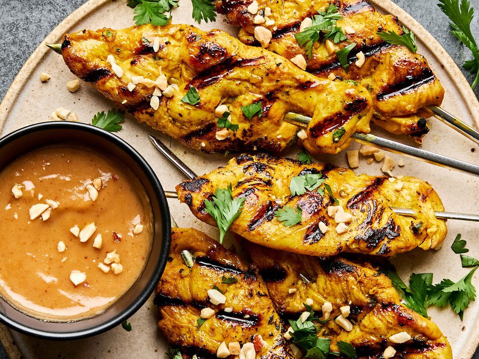 Grilled chicken satay skewers served with creamy peanut sauce, garnished with cilantro and crushed peanuts