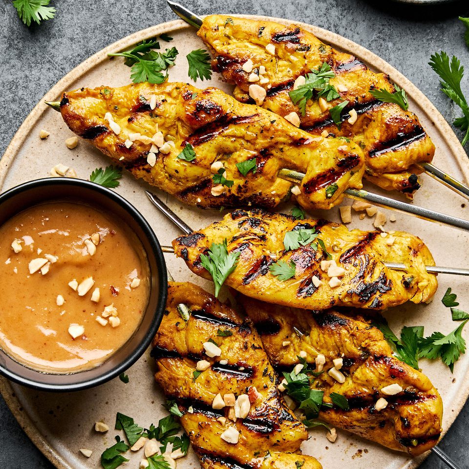 Grilled chicken satay skewers served with creamy peanut sauce, garnished with cilantro and crushed peanuts
