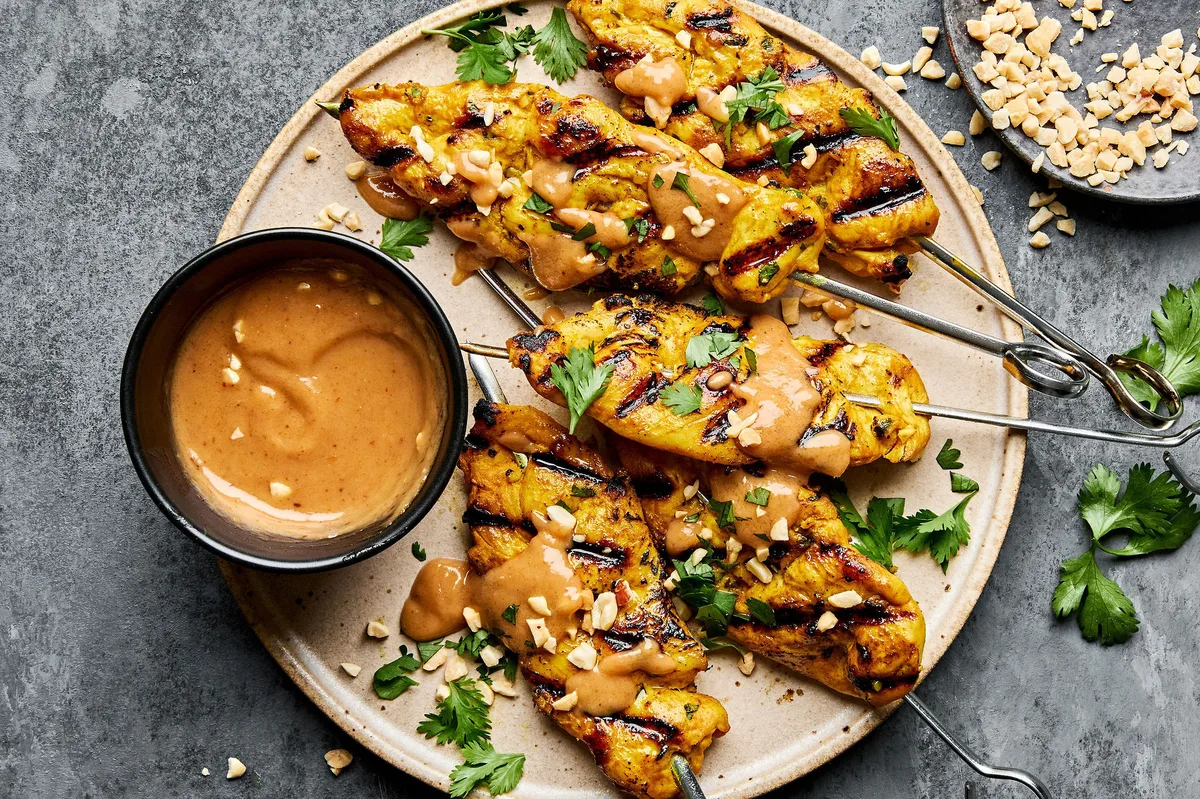 Grilled chicken satay skewers served with creamy peanut sauce, garnished with cilantro and crushed peanuts