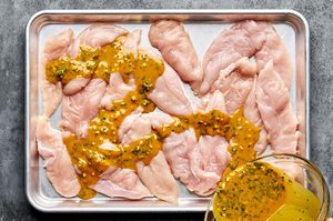 pounded raw chicken tenders being covered in a coconut milk, turmeric marinade