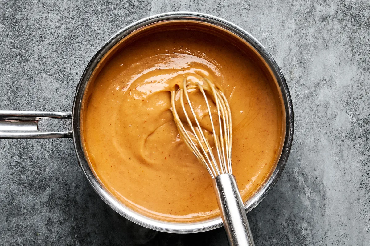 Homemade Peanut sauce cooking in a pot, being whisked until smooth and creamy