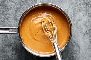 Homemade Peanut sauce cooking in a pot, being whisked until smooth and creamy
