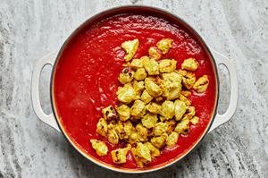 marinated, baked chicken being stirred into a pot with homemade tikka masala sauce
