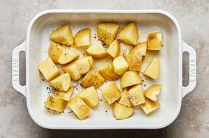 diced potatoes tossed with olive oil, salt & pepper in a baking dish ready to be roasted in the oven