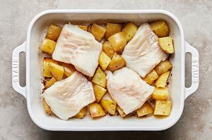 raw cod being laid on top of roasted potatoes in a baking dish