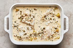 roasted potatoes topped with cod, covered in rosemary cream sauce in a baking dish ready to go in the oven