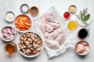 raw bone in chicken legs and thighs, red wine, vegetables, and spices in separate prep bowls laid out to make coq au vin