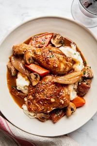 A plate of homemade coq au vin served over creamy mashed potatoes, garnished with herbs and vegetables.
