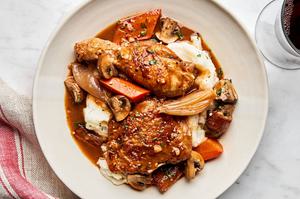 A plate of homemade coq au vin served over creamy mashed potatoes, garnished with herbs and vegetables.