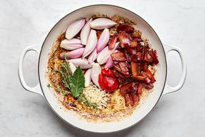 garlic, shallots, thyme, bay leaf, tomato paste, and bacon being cooked together in a pan