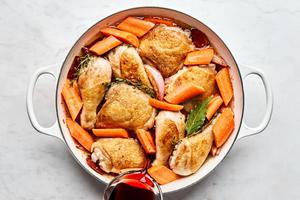 red wine being added to a pan of seared chicken and vegetables