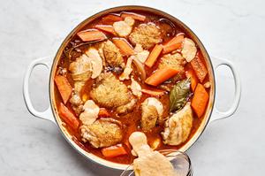 chicken stock and wine being added to a pan of chicken and vegetables to make coq au vin