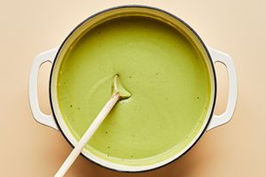 a pot of cream of broccoli soup being stirred with a wooden spoon