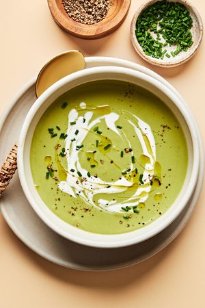 a bowl of homemade cream of broccoli soup sprinkled with chives and garnished with a swirl of cream served with crusty bread