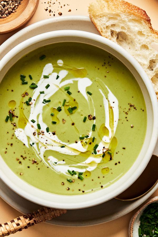 a bowl of homemade cream of broccoli soup sprinkled with chives and garnished with a swirl of cream served with crusty bread