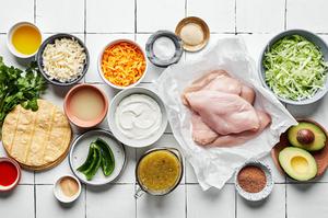 raw chicken breast, cheese, sour cream, salsa verde, spices, corn tortillas, olive oil, avocado and lettuce in prep bowls