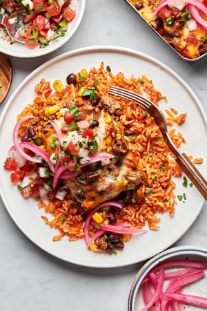 enchilada casserole served on top of mexican rice topped with pico de gallo and pickled onions on a plate with a fork