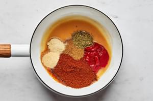 oil, flour, chili powder, garlic powder, onion powder, cumin, oregano, and tomato paste in a pot to make enchilada sauce