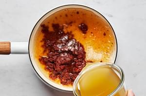 chicken broth being added to a pot with oil, flour, chili powder, garlic powder, onion powder, cumin, oregano & tomato paste