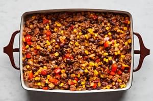 corn tortillas dipped in enchilada sauce topped with ground beef enchilada mixture in a casserole dish