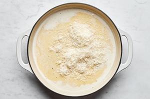Parmesan being added to a skillet with heavy cream to make Alfredo sauce.