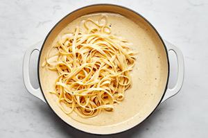 Homemade alfredo sauce in a skillet with cooked fettuccine noodles being stirred in