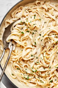Homemade fettuccine alfredo in a skillet sprinkled with fresh parsley with a serving spoons in it
