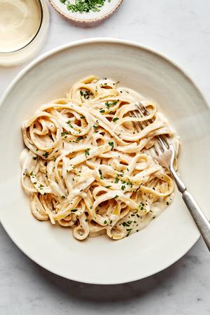 A bowl of homemade fettuccine Alfredo sprinkled with fresh parsley with a fork in it