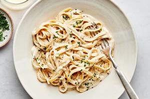 A bowl of homemade fettuccine Alfredo with noodles sprinkled with fresh parsley with a fork in it